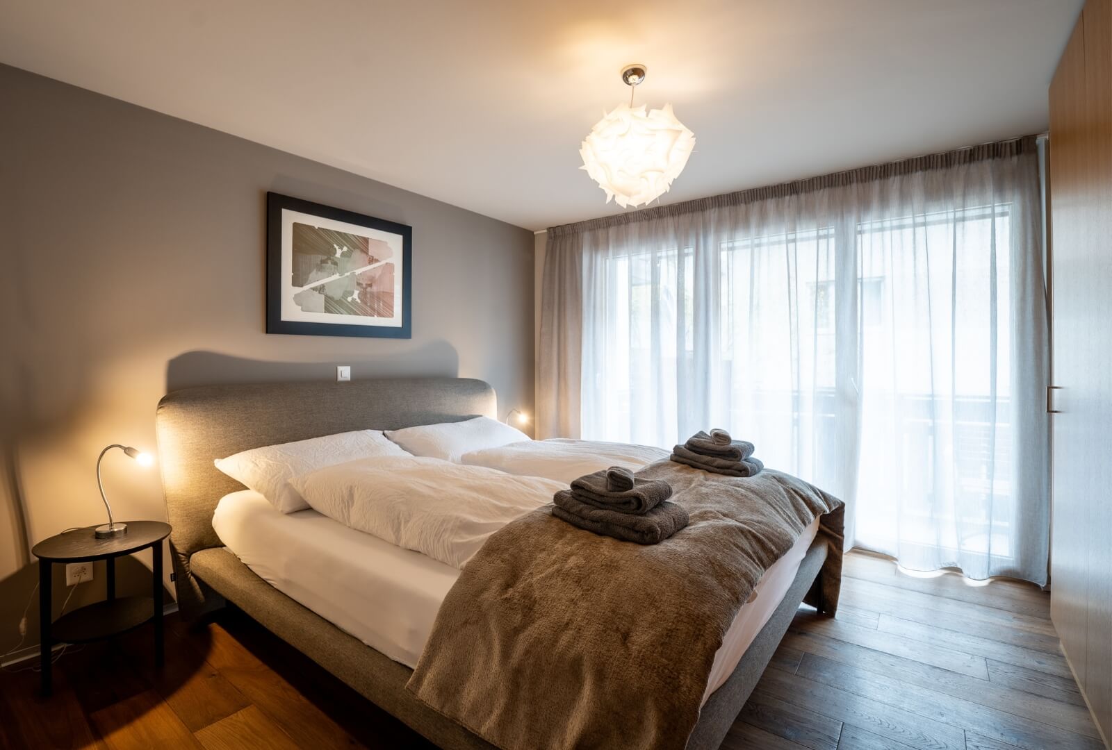 Cozy bedroom with double bed, bedside lamps and balcony access in Zermatt apartment