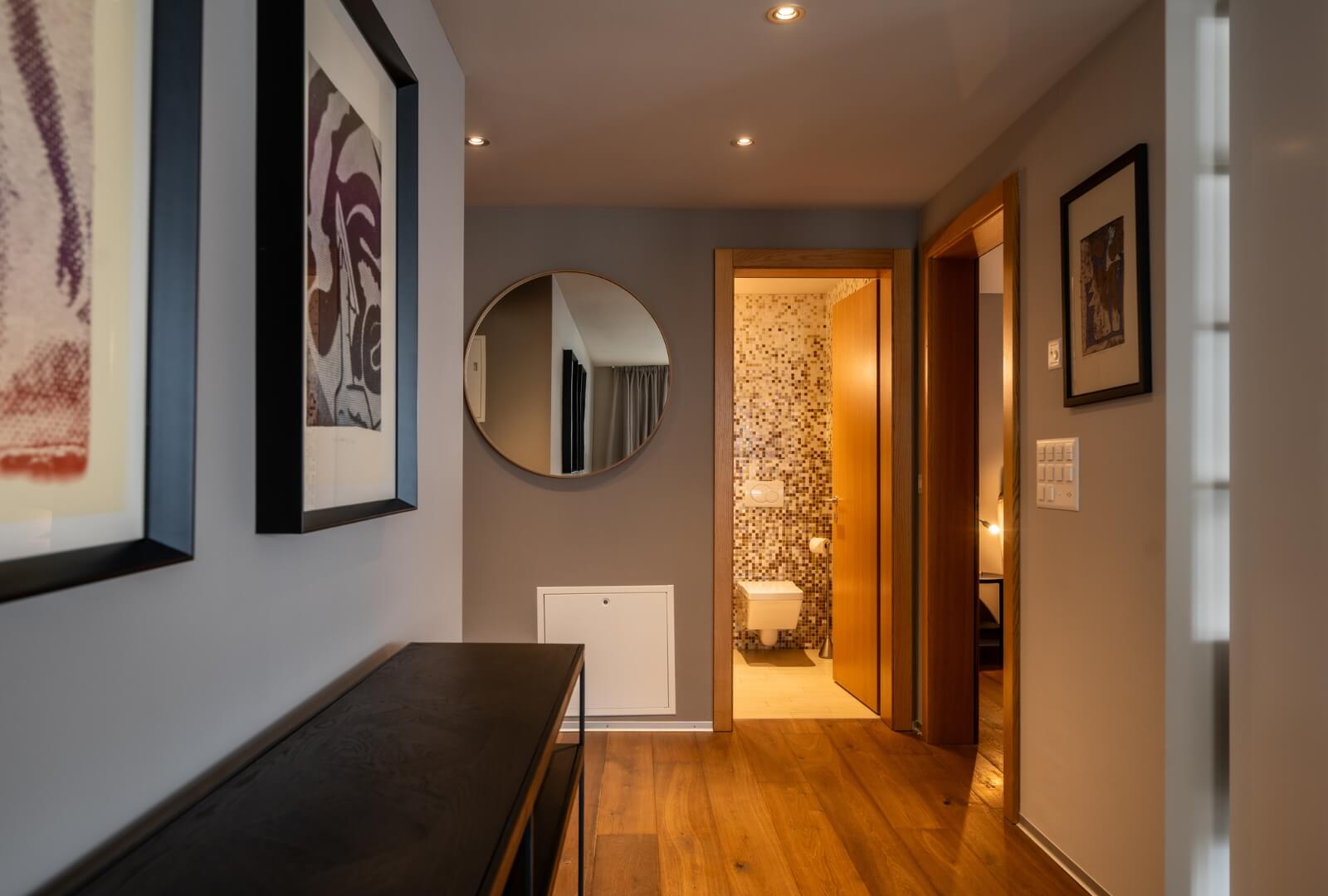 Stylish hallway with framed artwork and round mirror leading to modern bathroom
