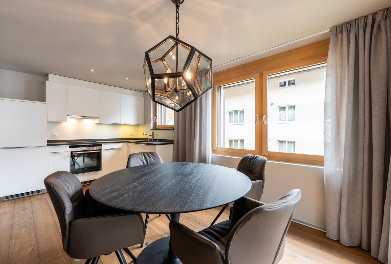 Modern open kitchen with dining table, leather chairs and design chandelier in Zermatt
