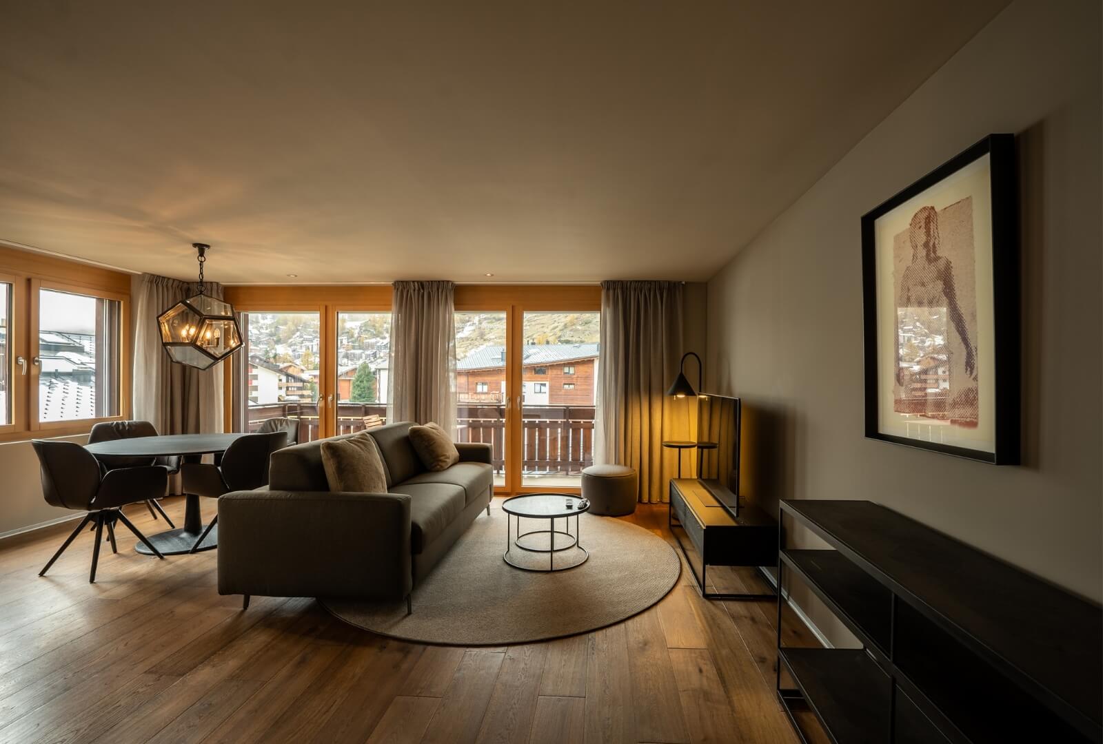 Spacious living room with sofa, dining area and balcony overlooking Zermatt rooftops