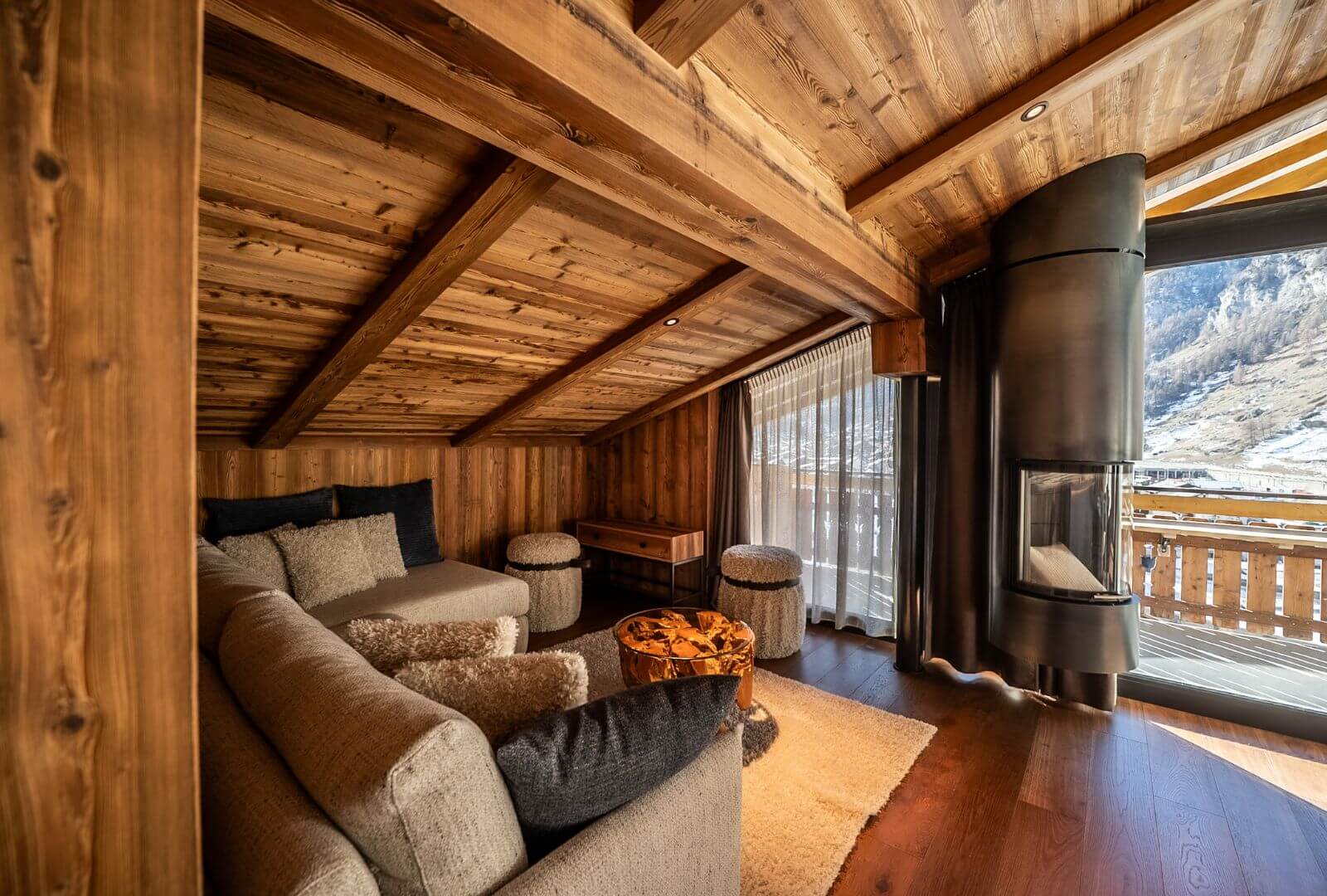 Spacious alpine living room at Viscaria Penthouse in Zermatt with wood beams, corner sofa and fireplace