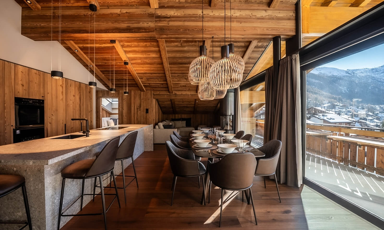 Open plan kitchen and dining area at Viscaria Penthouse Zermatt with wooden ceiling and mountain views from the balcony